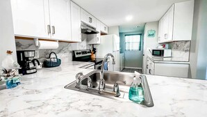 Une cuisine moderne avec des meubles blancs, un évier en acier inoxydable et un plan de travail en marbre.