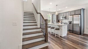 A modern kitchen with a central island, stainless steel appliances, and a wooden staircase. - College & Mimosa House in Downtown Auburn, less than 1 mile to Toomer's (Auburn)