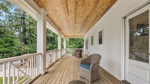 A covered porch with a wooden ceiling, white railings, and a wicker chair with a blue cushion. - College & Mimosa House in Downtown Auburn, less than 1 mile to Toomer's (Auburn)