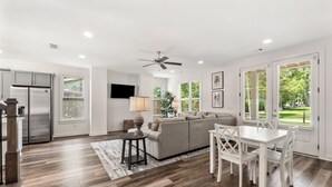 A modern kitchen with a built-in refrigerator, a dining area with a white table and chairs, a gray sofa, and a ceiling fan. - College & Mimosa House in Downtown Auburn, less than 1 mile to Toomer's (Auburn)