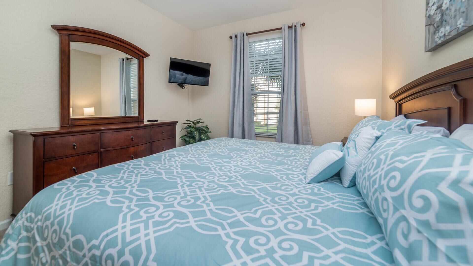 A bedroom with a bed, a dresser, a TV, and a window with curtains.