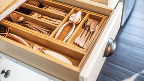 A kitchen with wooden countertops, a drawer organizer with utensils, and a stainless steel refrigerator.