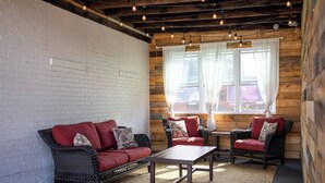 A cozy room with a brick wall, wooden beams, and a window with sheer curtains. There are two wicker sofas and a small table.