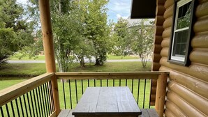 A wooden deck with a picnic table and benches, surrounded by a railing and a view of a grassy area and trees.