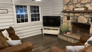 A cozy living room with a stone fireplace, a large flat-screen TV, and comfortable seating.