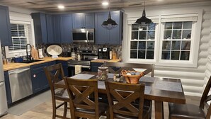 A modern kitchen with dark blue cabinets, stainless steel appliances, and a wooden dining table with four chairs.