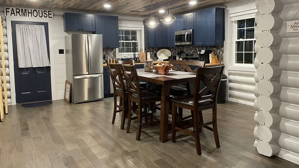 A kitchen with dark blue cabinets, stainless steel appliances, and a wooden dining table with chairs.