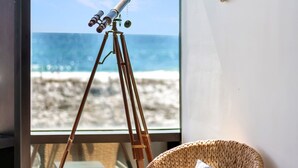 A room with a large window overlooking a beach, a telescope on a tripod, and a wicker chair with cushions. - Coastal Haven by Gulf and Sound (Pensacola Beach)