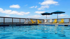 A swimming pool with clear blue water, yellow chairs, and blue umbrellas. - Coastal Haven by Gulf and Sound (Pensacola Beach)
