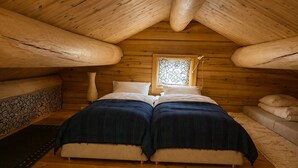 Un dormitorio acogedor con techo de madera, una cama con ropa oscura, una ventana con diseño floral y una mesita de noche con un florero.