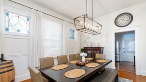 Une salle à manger avec une table en bois foncé, des chaises de couleur beige, des sets de table en fibres tressées et un luminaire suspendu.