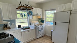 Une cuisine avec des meubles blancs, une cuisinière, un réfrigérateur et des casseroles suspendues.
