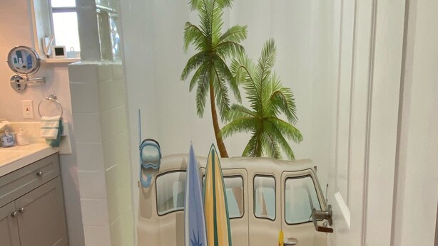 Une salle de bain avec un rideau de douche orné d'un motif représentant un van, des planches de surf et des palmiers.
