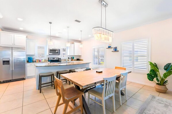 Une cuisine moderne avec des meubles blancs, un îlot central et un coin repas comprenant une table et des chaises en bois.