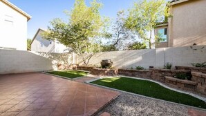 Un espace patio doté d’un sol carrelé, d’une petite pelouse et d’un jardinier en pierre contenant un grand pot.