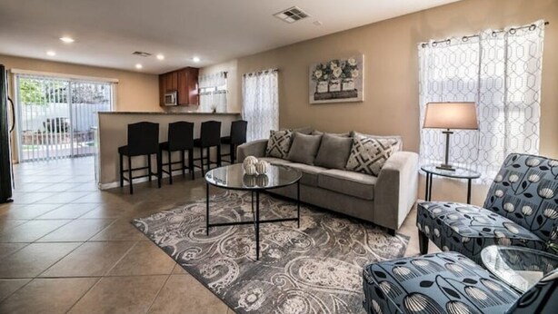 Un salon comprenant un canapé, une table basse et des fauteuils à motifs. Il y a également un coin cuisine avec des placards et un four à micro-ondes.