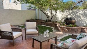 Une terrasse extérieure avec deux fauteuils en osier, une table en bois et un petit coin jardin agrémenté d’un arbre et d’un jardinière.