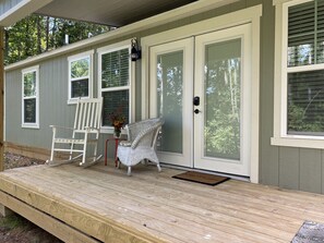 A covered porch with a bench and a chair, a door with a doormat, and windows with blinds.