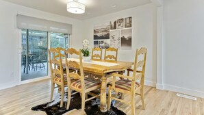 A dining area with a wooden table and chairs, a black and white rug, and a ceiling light fixture.