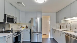 A modern kitchen with stainless steel appliances, grey cabinetry, and a bright overhead light.