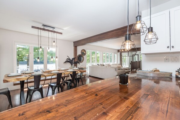Una cocina amplia con una isla grande de madera, lámparas colgantes modernas y vistas al exterior a través de ventanas grandes.