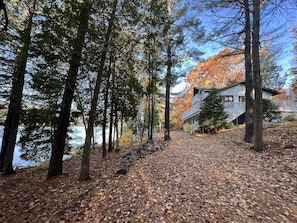 A cabin with a porch and a staircase leading up to it, surrounded by trees and a lake.