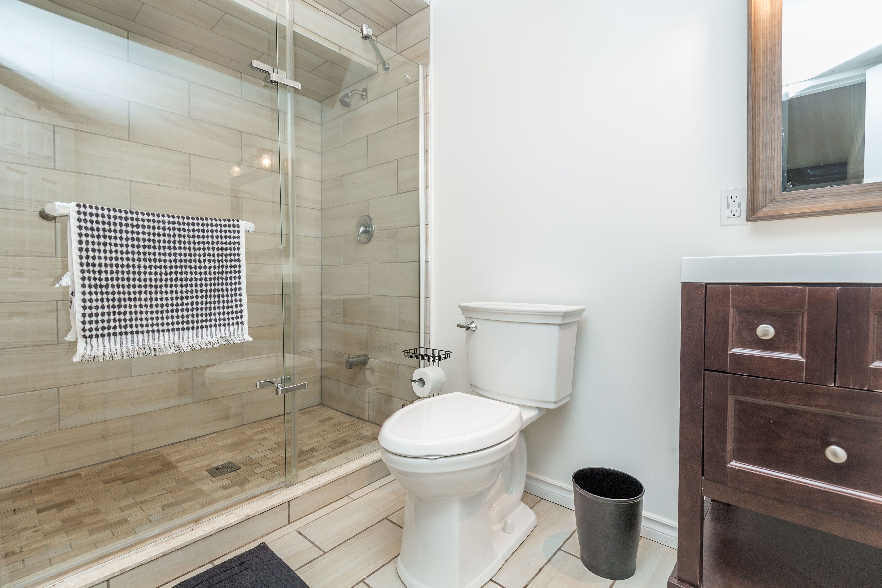 A modern bathroom with a glass shower enclosure, a white toilet, and a wooden vanity with drawers.