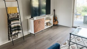 A living room with a flat-screen TV on a white cabinet, a guitar, a glass coffee table, and a patterned rug. - Modern Guest Suite, 3 Miles from Downtown Bozeman (Bozeman)