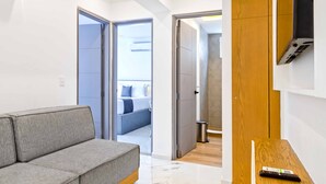 Una habitación de hotel moderna con un sofá gris, un mueble de madera y un televisor montado en la pared.