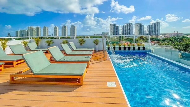 Zona de piscina en la azotea con sillones y el horizonte de la ciudad al fondo.