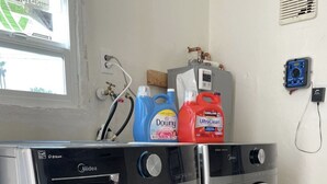 A front-loading Midea washer and dryer in a laundry room with a window, a water heater, and detergent bottles.