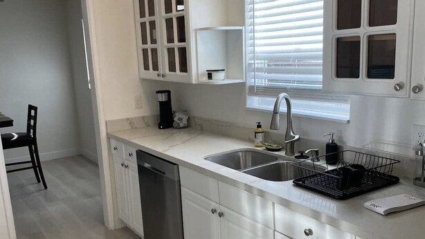 A modern kitchen with white cabinetry, a dishwasher, a double sink, and a window with blinds.