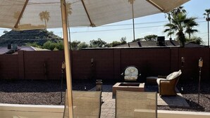 An outdoor patio with a round glass table, wicker chairs, and a large umbrella.