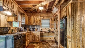A rustic kitchen with wooden cabinets, a stove, a microwave, and a refrigerator. - The Log Castle~Stunning Mountain Views~Hot Tub (Sevierville)