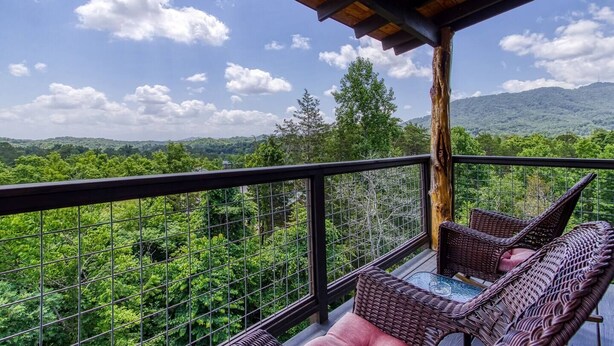 A balcony with wicker furniture, a metal railing, and a view of a forested landscape with mountains in the distance. - The Log Castle~Stunning Mountain Views~Hot Tub (Sevierville)