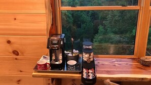 A wooden cabin interior with a coffee maker, mugs, and a jar of snacks on a table by a window overlooking a forest. - The Log Castle~Stunning Mountain Views~Hot Tub (Sevierville)