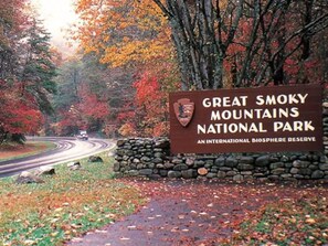 A sign for Great Smoky Mountains National Park with a stone wall and a road curving through a forest.