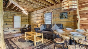 A log cabin interior with a wooden ceiling, a sofa set, a coffee table, a dining table with chairs, and a hanging light fixture. - The Log Castle~Stunning Mountain Views~Hot Tub (Sevierville)