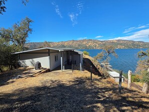 Une cabane dotée d’un porche abrité, d’un barbecue et offrant une vue sur un lac et des collines.