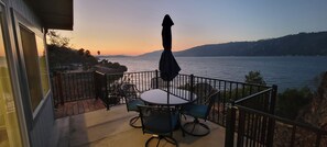 A balcony with a table and chairs, overlooking a body of water and hills.