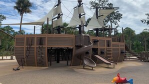 Estructura de juegos temática de piratas, con un tobogán, pared de escalada y torre de vigilancia.
