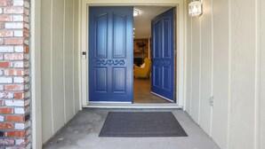 Una porta blu con un pannello decorativo, una sedia gialla all'interno e un muro in mattoni a sinistra.
