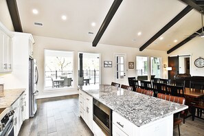 A spacious kitchen with a large island, white cabinetry, and a dining area with chairs and a table. - Dawg House, Private Pool, Wi-Fi, @ Frio River Vacation Rentals (Concan)