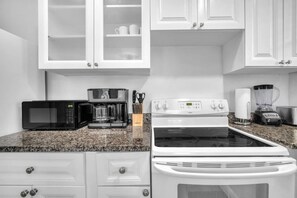 A kitchen with white cabinets, a microwave, a coffee maker, a stove, and a blender.