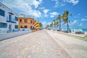 A hotel with a paved walkway, palm trees, and a clear sky.
