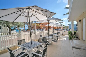 An outdoor patio with tables and umbrellas, a white fence, and buildings in the background. - Amazing 1st Floor Apartment Just Steps to Beach (Hollywood)