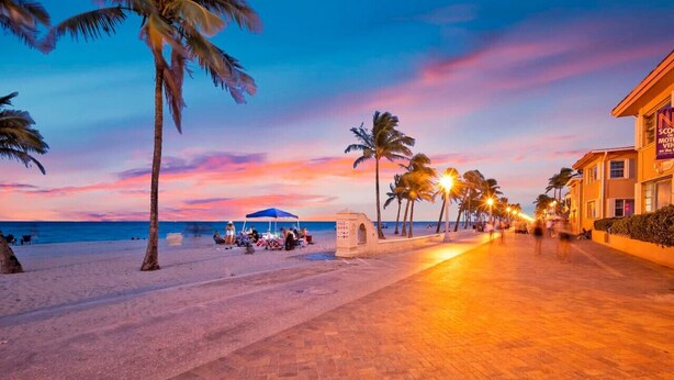Ein Strandhotel mit gepflastertem Weg, Palmen und einem Sonnenuntergangshimmel.