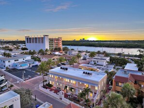 A hotel with multiple floors, a parking lot, and a view of the ocean at sunset.