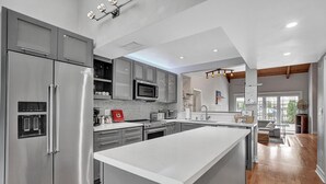 Een moderne keuken met roestvrijstalen apparatuur, een groot eiland en uitzicht op de woonkamer.