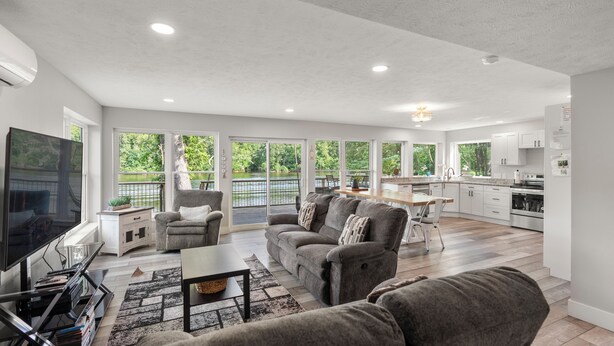 A spacious living area with a large TV, grey sofas, and a kitchen in the background. - River Retreat W/ HOT TUB/ Game room (Bristol)